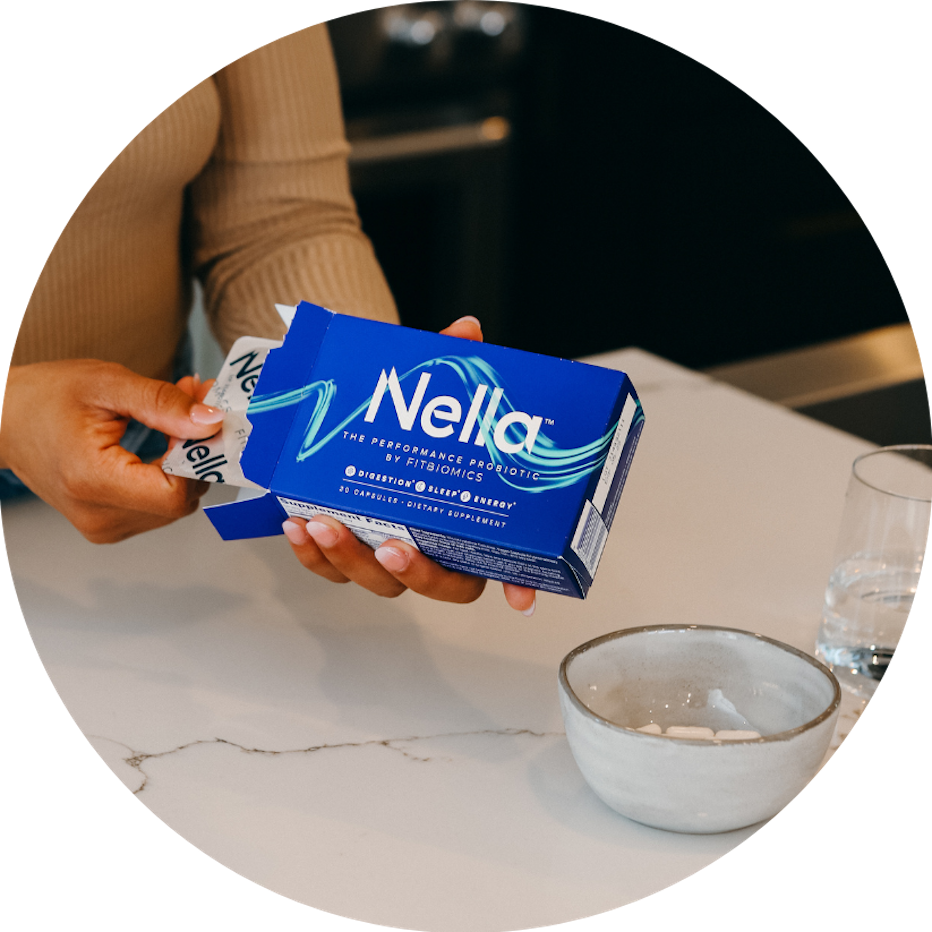 woman pulling blister card out of a box of nella next to a bowl of capsules and glass of water