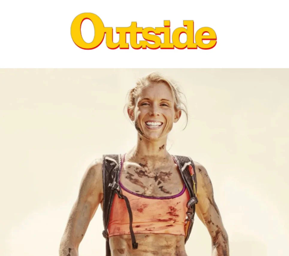 A woman athlete covered in dirt, smiling broadly under Outside logo